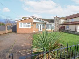 A brick bungalow with a stone chimney and a driveway next to a green lawn at Greenacres in Towyn