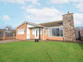 A single story brick house with large windows a stone chimney and a green lawn at Greenacres in Towyn
