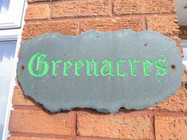 A stone plaque with green text reading Greenacres mounted on a brick wall at Greenacres in Towyn