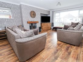 A living room with two sofas a wooden floor a TV on a wooden cabinet a wall clock and a fireplace at Greenacres in Towyn