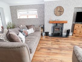 A living room with a gray sofa wooden floor a wood-burning stove and a wooden cabinet at Greenacres in Towyn