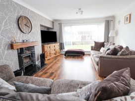 A living room with sofas a wooden cabinet a large television a fireplace and a large window at Greenacres in Towyn