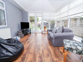 A living room with a sofa and chairs a television and wooden flooring at Greenacres in Towyn