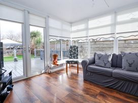 A conservatory with wooden floor a sofa with cushions a patterned chair and a door leading to a deck at Greenacres in Towyn