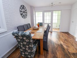 A dining room with a wooden table and six chairs two with floral covers and a large wall clock at Greenacres in Towyn
