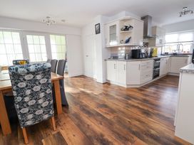 A kitchen and dining area with wooden flooring and white cabinets at Greenacres in Towyn