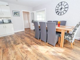 A dining area with a wooden table and six chairs with a large wall clock and kitchen cabinets at Greenacres in Towyn