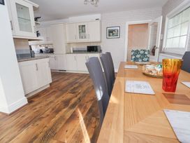 A kitchen and dining area with wooden flooring white cabinets and a dining table with chairs at Greenacres in Towyn