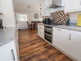 A kitchen with white cabinets a stove and a tiled backsplash opening into a dining area with a wooden table and chairs at Greenacres in Towyn
