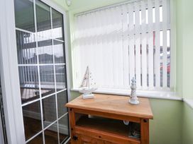 A wooden cabinet with decorative ship and lighthouse figurines in front of a window with vertical blinds at Greenacres in Towyn