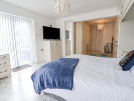 A bedroom with a bed covered in white bedding and a blue throw a television on a cabinet a tall mirror wardrobes and vertical blinds on a sliding door at Greenacres in Towyn