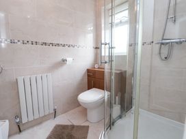 A bathroom with a toilet, radiator, wooden cabinet, shower enclosure, and tiled walls at Greenacres in Towyn
