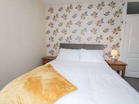 A bedroom with a bed white bedding yellow blanket two wooden nightstands and a floral wallpaper at Greenacres in Towyn