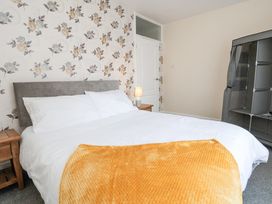 A bedroom with a bed a wooden side table with a lamp floral wallpaper and a grey storage unit at Greenacres in Towyn