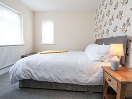 A bedroom with a bed with white bedding beside a wooden nightstand with a lamp at Greenacres in Towyn