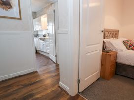 View of a hallway with wooden floor leading to a kitchen with white cabinets and a bedroom with a bed and bedside table at Greenacres in Towyn