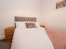 A bedroom with a bed with a tufted headboard white bedding a colorful pillow and a pink throw blanket with two nightstands and a painting on the wall at Greenacres in Towyn