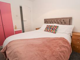 A bedroom with a bed with a tufted headboard colorful pillow pink blanket wooden bedside tables and pink wardrobe at Greenacres in Towyn