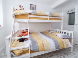 A white bunk bed with stuffed animals on the lower bed and striped bedding in a room at Greenacres in Towyn