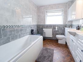 A bathroom with a bathtub, toilet, sink, cabinets, and a window at Greenacres in Towyn