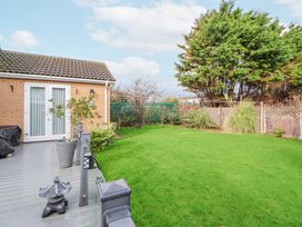 A backyard with a green lawn a wooden deck and a small brick building at Greenacres in Towyn