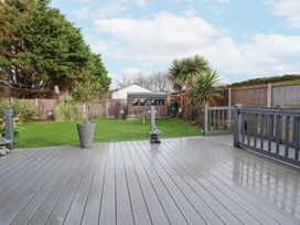 A garden with a wooden shed and trees viewed from a grey wooden deck with potted plants and a fenced yard at Greenacres in Towyn