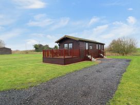 A wooden cabin with a deck and steps surrounded by grass with a gravel driveway at Cuckoo in Ramsey Huntingdon