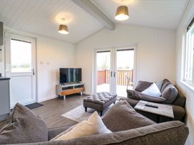 A living room with a gray sofa a matching ottoman a small TV on a stand and glass doors leading outside at Cuckoo in Ramsey Huntingdon