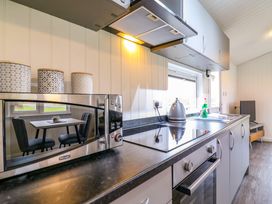 A kitchen countertop with a microwave oven, three patterned containers, a kettle, a stove, a sink, and a window showing a dining table with chairs at Cuckoo in Ramsey Huntingdon
