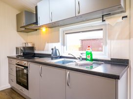 A kitchen with grey cabinets a microwave a kettle a sink and a window at Cuckoo Ramsey Huntingdon