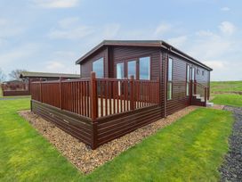 A brown wooden cabin with a deck and railings on a grassy plot at Kingfisher in Ramsey Huntingdon