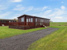 A brown wooden cabin with a deck and gravel pathway surrounded by grass at Kingfisher in Ramsey Huntingdon