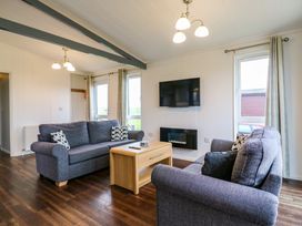 A living room with two sofas a central wooden coffee table a wall-mounted television and an electric fireplace at Kingfisher Ramsey Huntingdon