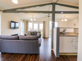 A living room with gray sofas a wall-mounted TV and a kitchen counter with mugs at Kingfisher Ramsey Huntingdon