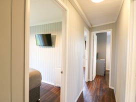 A hallway with doors leading to rooms with wall mounted televisions and wooden floors at Kingfisher in Ramsey Huntingdon
