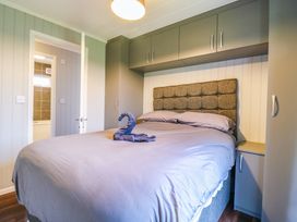 A bedroom with a double bed featuring a fabric headboard and grey bedding with overhead and side cabinets at Kingfisher Ramsey Huntingdon