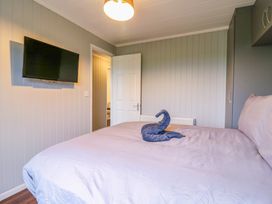 A bedroom with a bed featuring a towel shaped like an animal a wall mounted television and an open door at Kingfisher in Ramsey Huntingdon