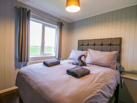 A bedroom with a bed covered in white sheets and gray towels by a window with gray curtains at Kingfisher in Ramsey Huntingdon