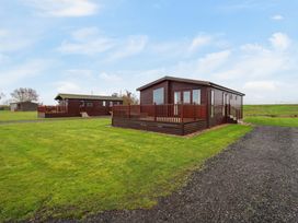 Two wooden cabins with decks on a grassy field under a blue sky at Kingfisher in Ramsey Huntingdon