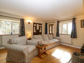 A living room with striped sofas wooden floor and floral curtains at Court House Cottage in Gatcombe near Blakeney