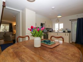 A kitchen with cream cabinets a wooden dining table with flowers and a chair at Court House Cottage Gatcombe near Blakeney