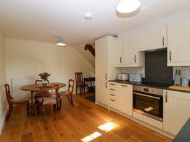 A kitchen with cream cabinets a wooden dining table with four chairs and flowers on it at Court House Cottage in Gatcombe near Blakeney
