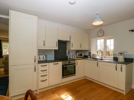 A kitchen with cream cabinets a black countertop a window a clock and various appliances at Court House Cottage in Gatcombe near Blakeney