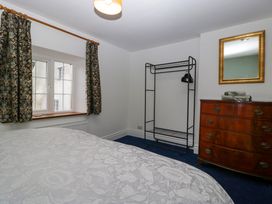 A bedroom with a bed covered by a patterned duvet a window with floral curtains a metal clothes rack and a wooden dresser with a mirror at Court House Cottage in Gatcombe near Blakeney