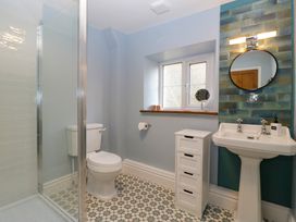 A bathroom with a toilet shower pedestal sink round mirror and small white storage unit at Court House Cottage Gatcombe near Blakeney
