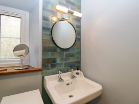 A bathroom sink with two taps a round mirror and a soap dispenser by a window at Court House Cottage in Gatcombe near Blakeney