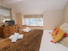A bedroom with a bed covered with a brown blanket and white towels on top a wooden dresser with a mirror and small television in the corner at Glandwr Cottage in Llanbedr