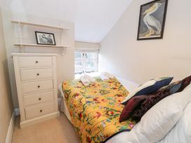A bedroom with a bed covered in a floral quilt and pillows a chest of drawers and bird paintings at Glandwr Cottage in Llanbedr