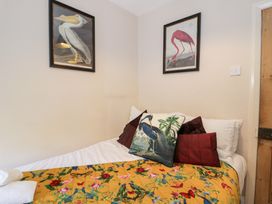 A bed with colorful bird and flower blanket and bird-themed pillows below two framed bird pictures at Glandwr Cottage in Llanbedr