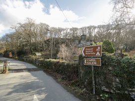A road with signs pointing to Rhaeadr Nantcol Waterfalls and Capel Salem with trees and stone walls at Glandwr Cottage in Llanbedr